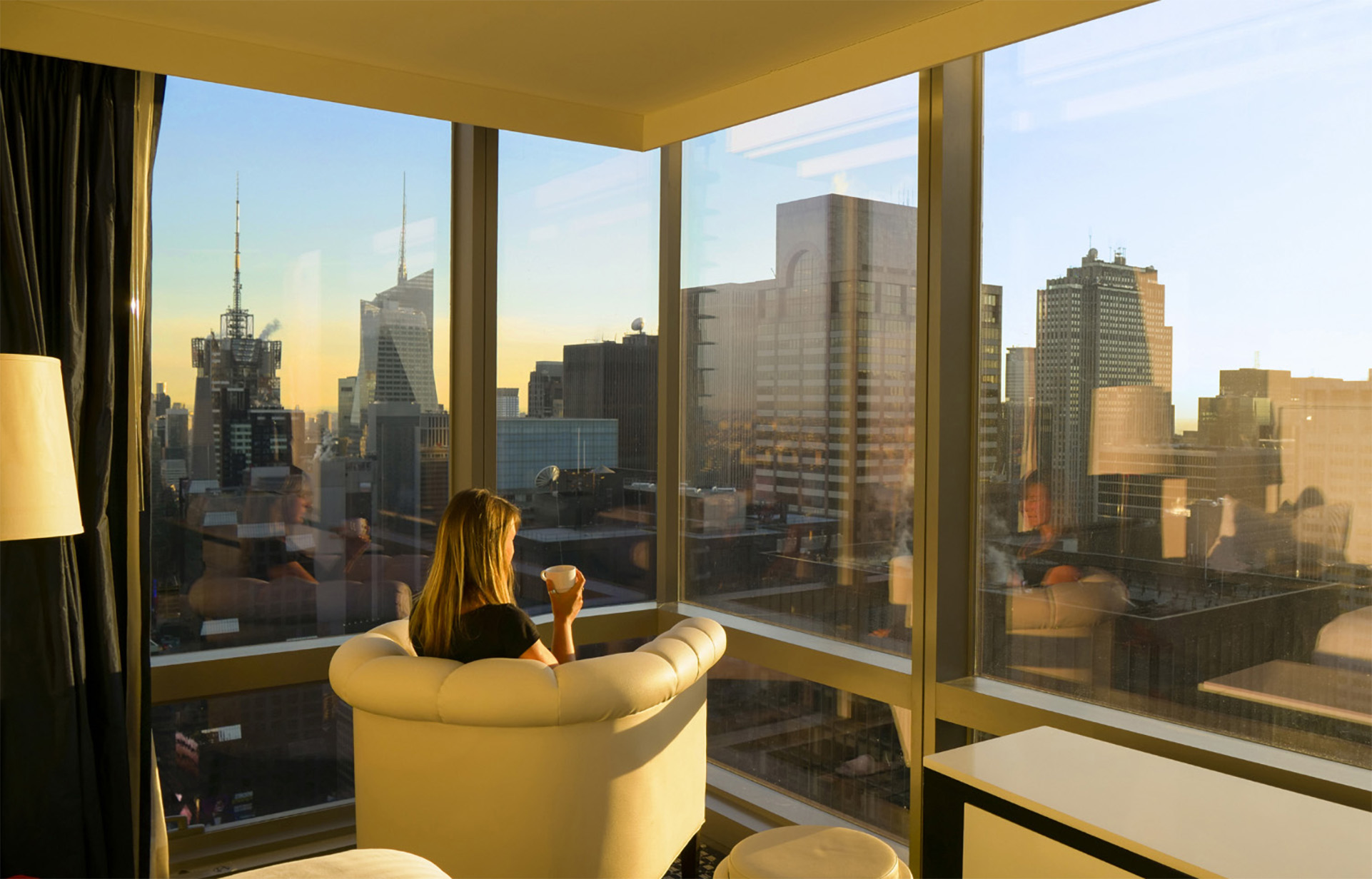 Woman in a NYC high rise drinking coffee looking out on the city