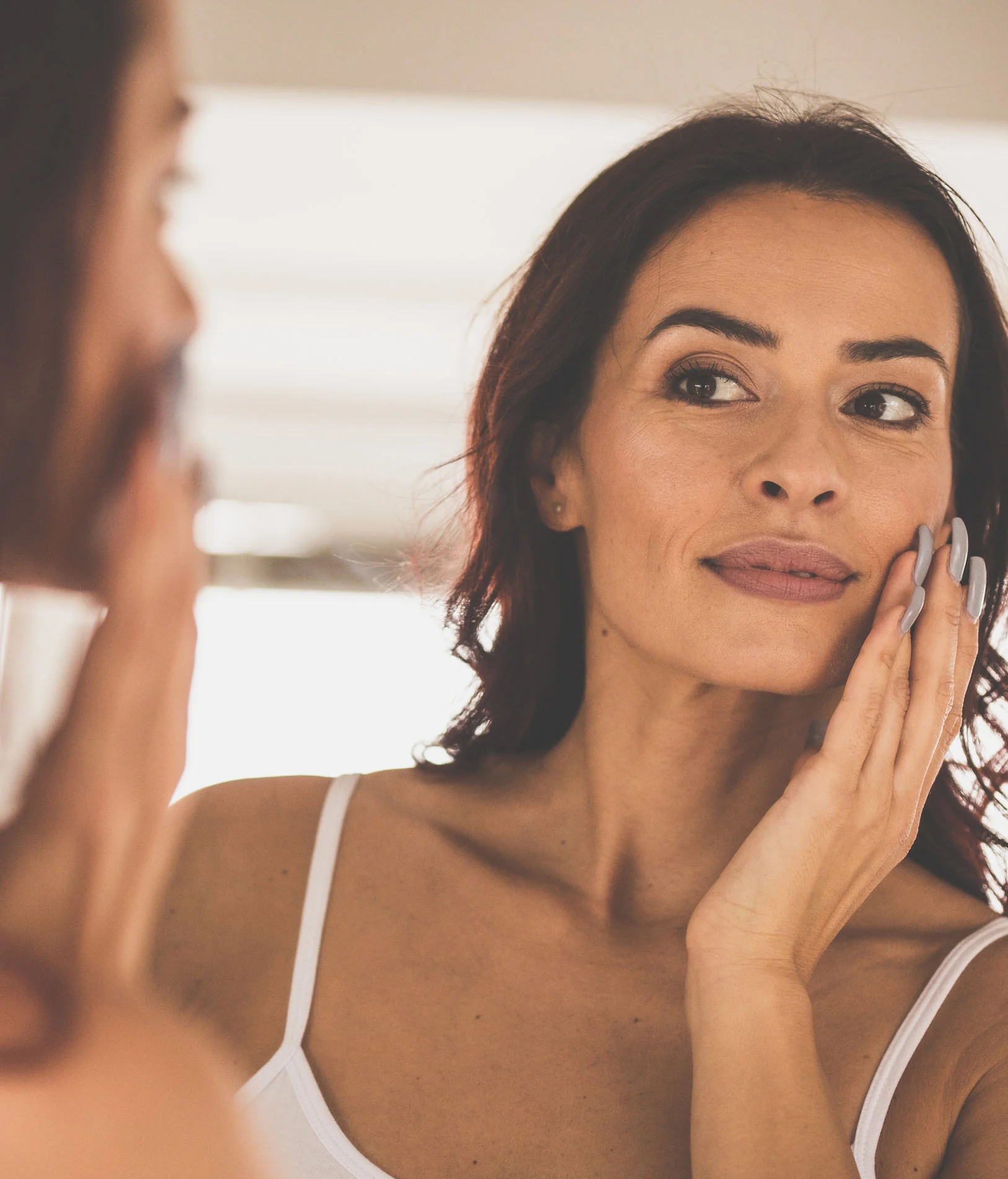 The benefits of Buccal Fat Removal - woman admiring her thin face in the mirror